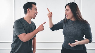 A man and a woman in grey shirts pointing fingers at each other