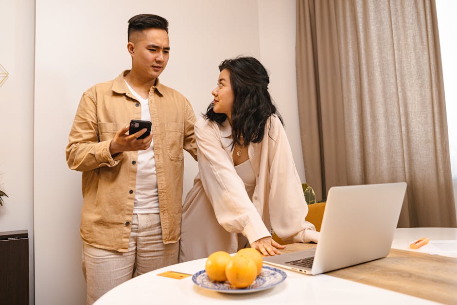 A couple in a modern home environment using a smartphone and laptop together.