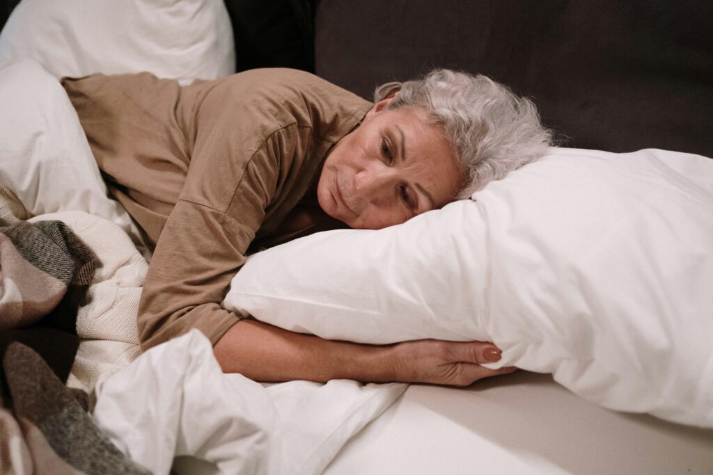 Senior woman lying on a pillow in bed, appearing thoughtful and calm.