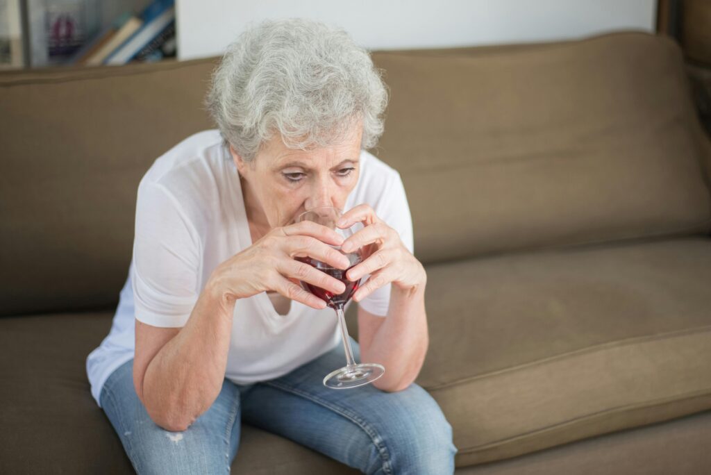 Senior woman in contemplation, drinking wine on a sofa, expressing solitude and reflection.